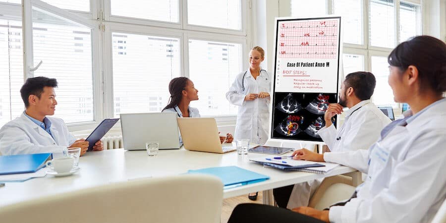 Medical team including doctors, nurses, and certified hypnotherapist collaborating in modern hospital conference room with patient care charts